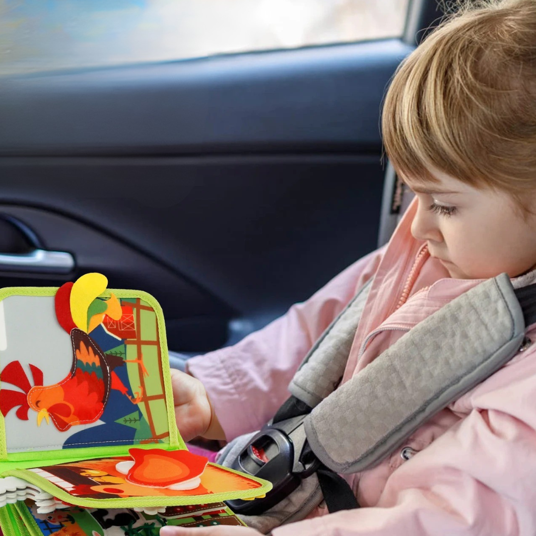 Dziecko w foteliku samochodowym przegląda kolorową książeczkę edukacyjną z kogutem.